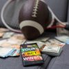 FootballR - NFL - Ein Mobiltelefon mit der Aufschrift NFL Wetten liegt auf einem Stapel Geld und einem Football.