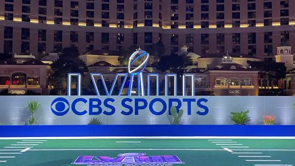 FootballR - NFL - Diese Beschreibung wurde automatisch generiert. Das CBS-Sportlogo befindet sich auf einem Footballfeld in Las Vegas. Super Bowl LVIII Tipping Game