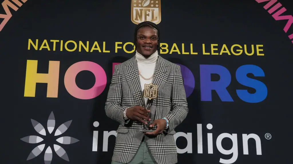 FootballR - NFL MVP Rennen 2024 - Diese Beschreibung wurde automatisch generiert. Lamar Jackson, der NFL MVP 2023, hält stolz seine Auszeichnung für seine bemerkenswerte Leistung in der National Football League.