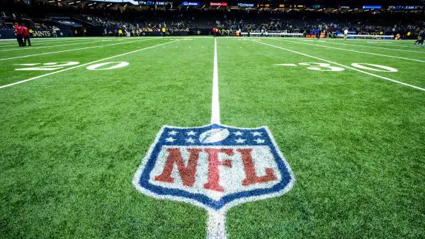 FootballR - NFL - Ein Footballfeld mit dem NFL-Logo in der Mitte zwischen der 20- und 30-Yard-Linie. Das Stadion ist beleuchtet und im Hintergrund voller Zuschauer. Eine Anzeigetafel zeigt „FINAL STATS“ für die Saison 2023 an. Das Feld hat deutlich erkennbare weiße Yard-Linien und Hash-Markierungen, was auf eine gut gepflegte Spielfläche hinweist. Diese Beschreibung wurde automatisch generiert.